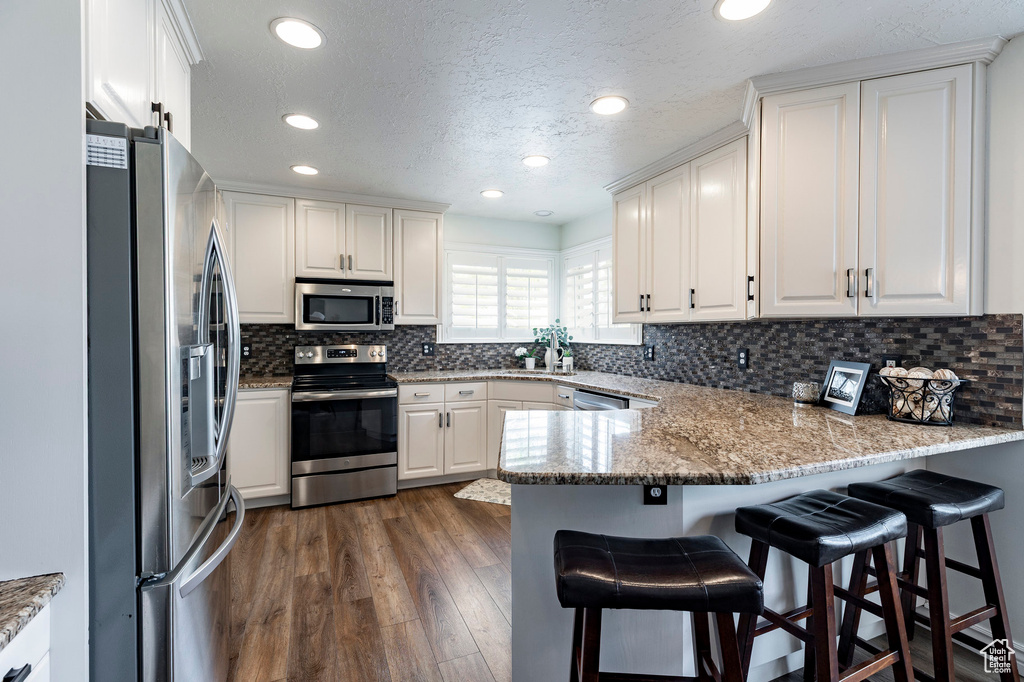 Kitchen with appliances with stainless steel finishes, a peninsula, and white cabinetry