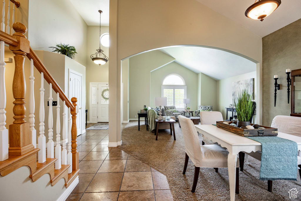 Dining room featuring arched walkways, high vaulted ceiling, carpet, stairs, and baseboards