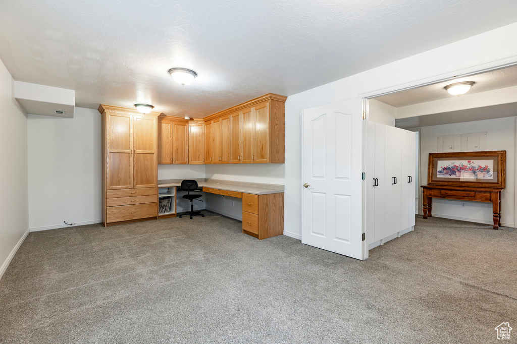 Home office with baseboards, light carpet, and built in desk