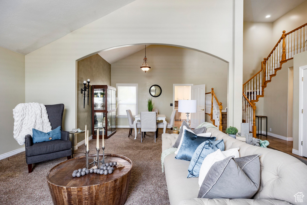Living area with arched walkways, stairs, baseboards, carpet floors, and vaulted ceiling
