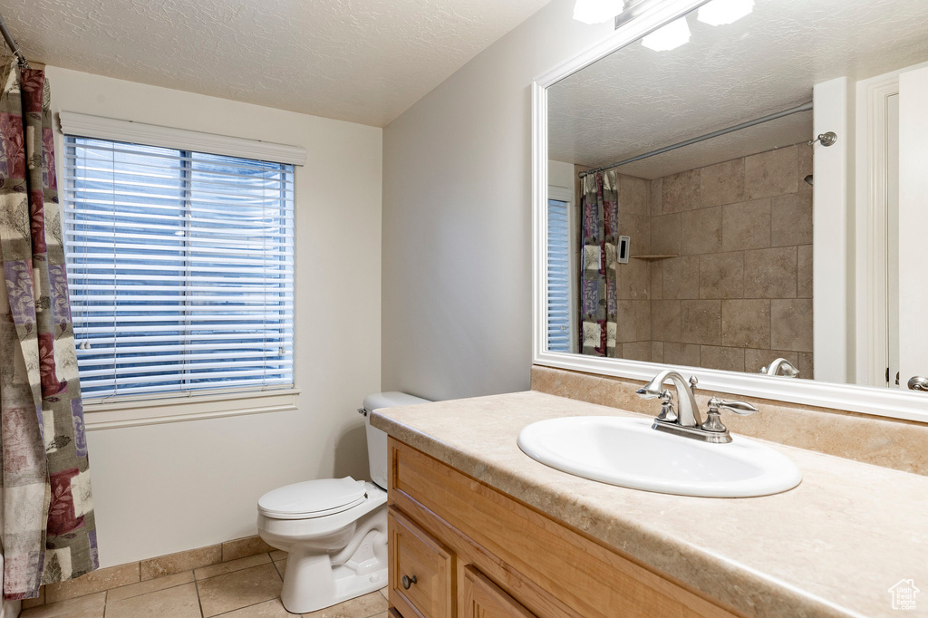 Full bathroom featuring a shower with curtain, a textured ceiling, tile patterned floors, vanity, and toilet