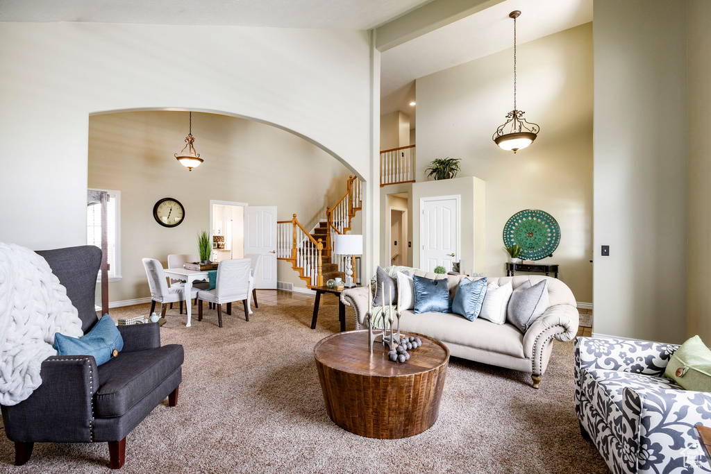 Living area with carpet floors, stairway, high vaulted ceiling, baseboards, and arched walkways