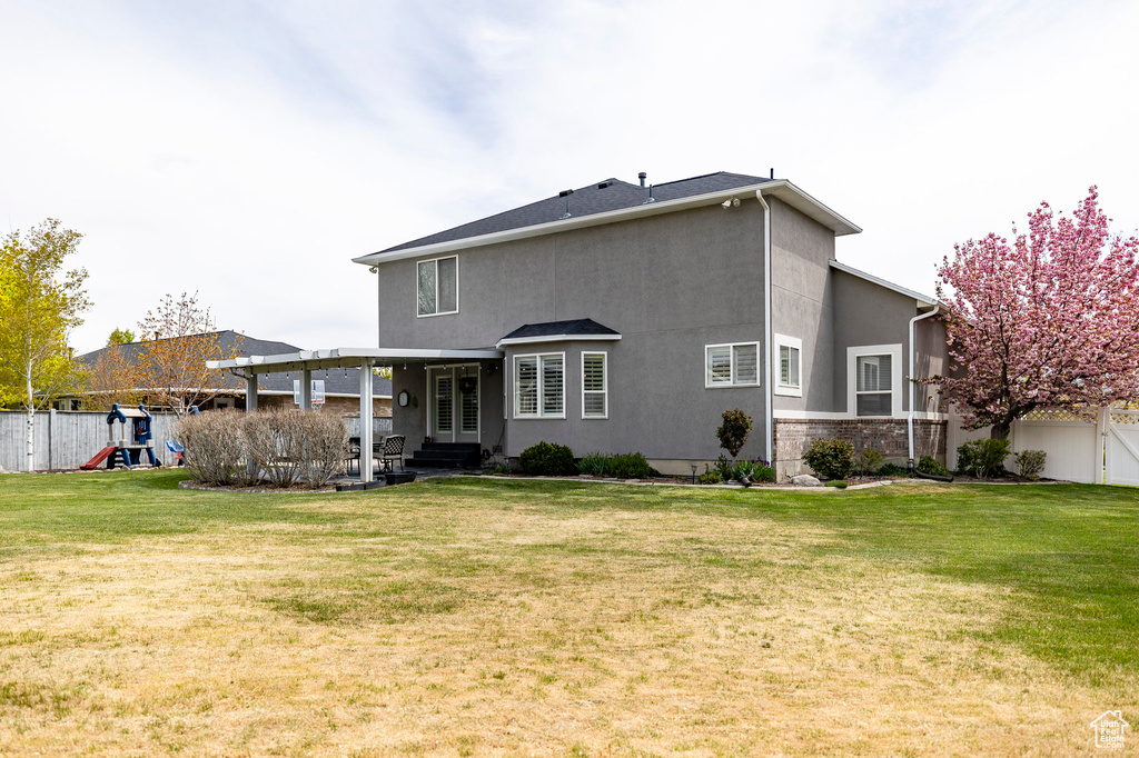 Rear view of property with a playground, stucco siding, a yard, and fence private yard
