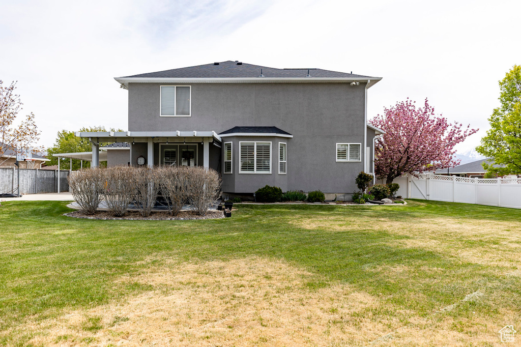 Rear view of house featuring a lawn, a fenced backyard, and stucco siding