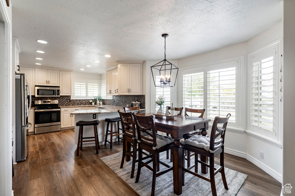 Dining room featuring a textured ceiling, baseboards, an inviting chandelier, recessed lighting, and dark wood-type flooring