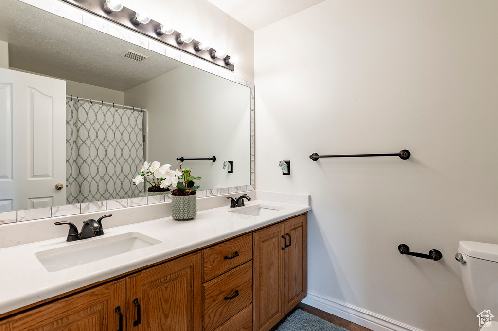 Full bath with double vanity, toilet, visible vents, and a sink