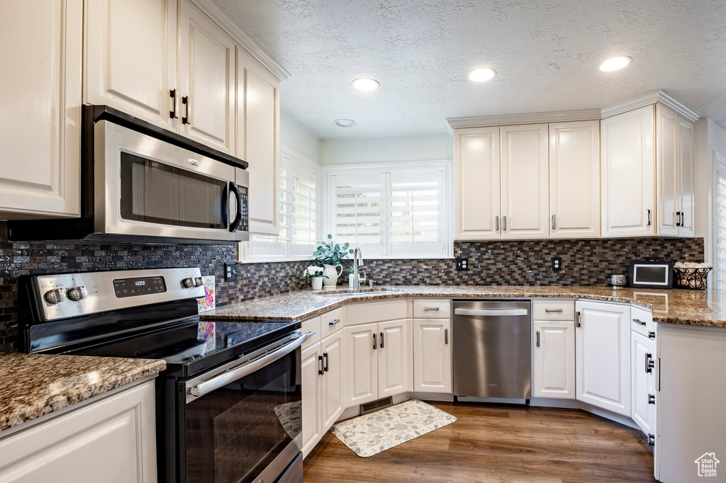 Kitchen featuring appliances with stainless steel finishes, a sink, backsplash, light stone counters, and recessed lighting