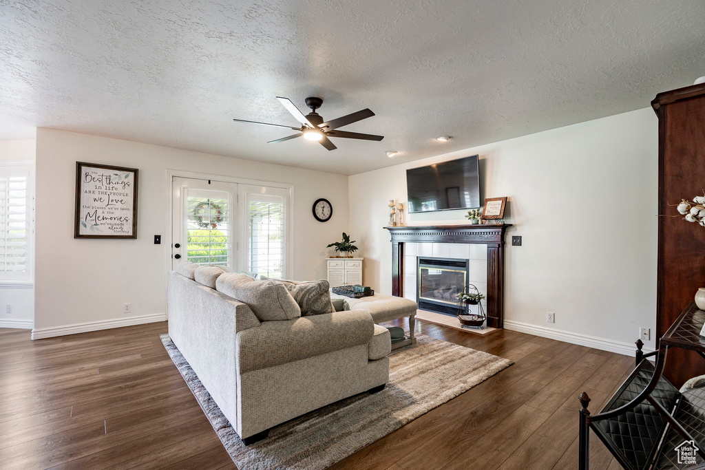 Living area with a textured ceiling, baseboards, dark wood-type flooring, a ceiling fan, and a tile fireplace