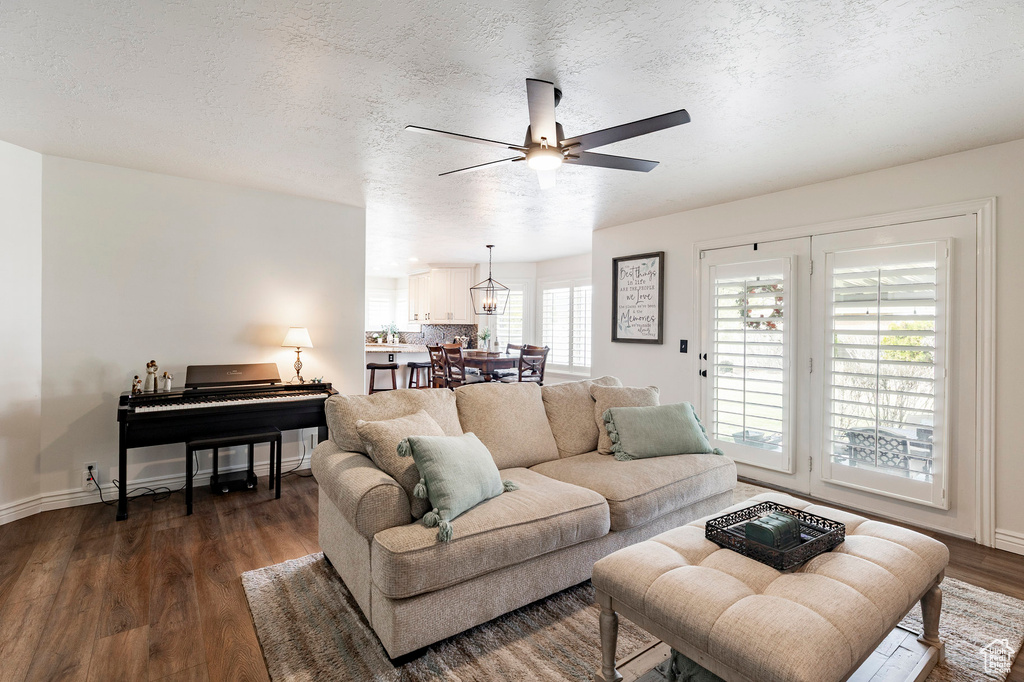 Living room with dark wood-style flooring, ceiling fan, baseboards, and a textured ceiling