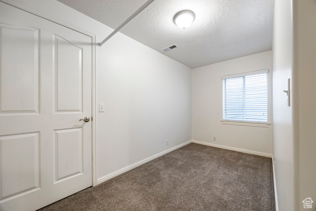 Spare room featuring dark carpet, a textured ceiling, and baseboards