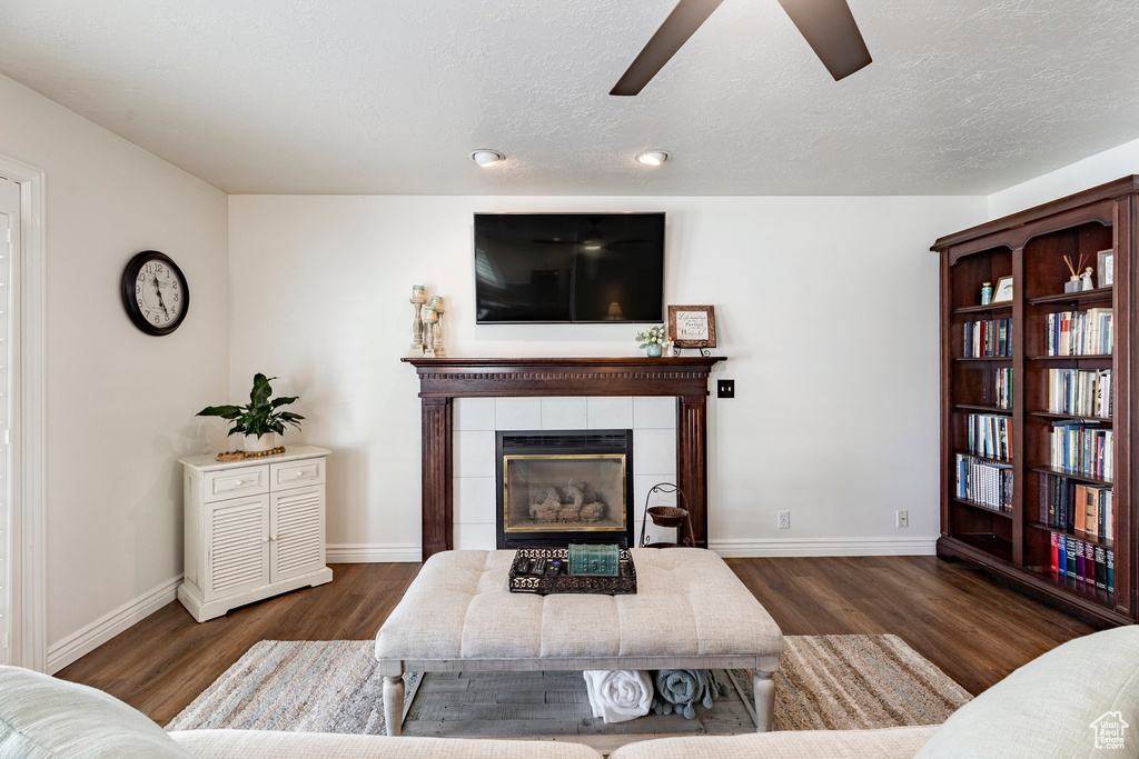 Living area with a tiled fireplace, baseboards, ceiling fan, and wood finished floors