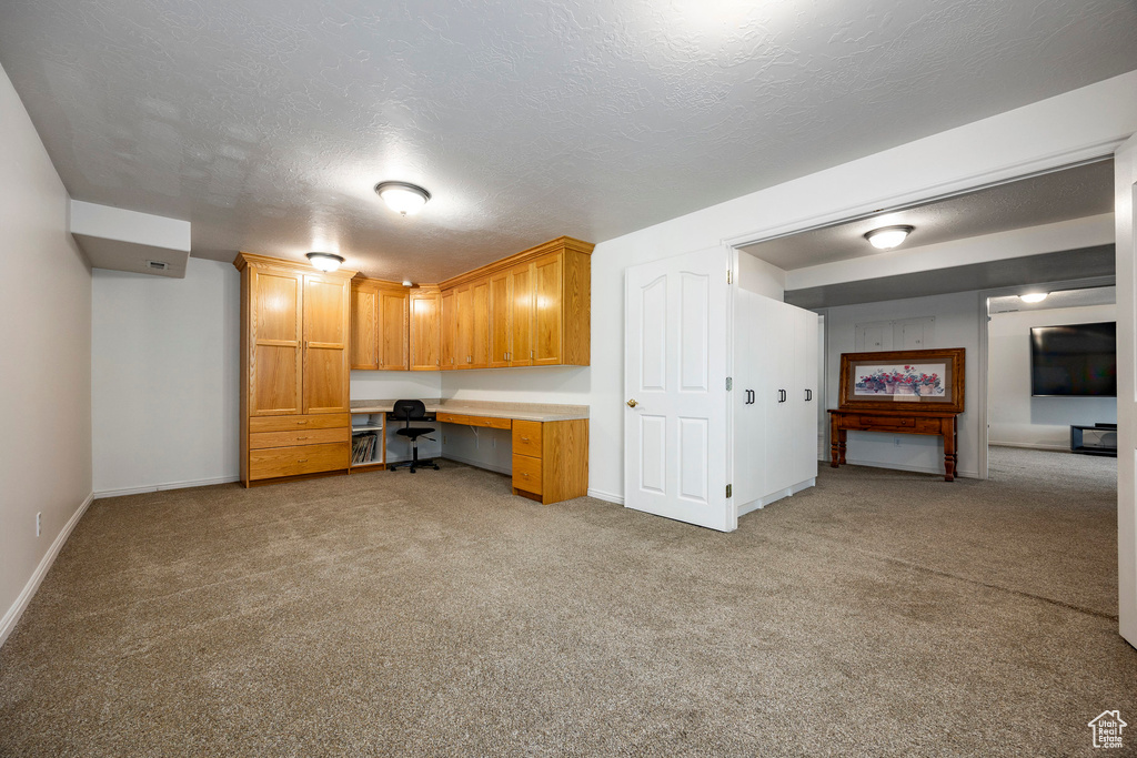 Unfurnished office featuring built in study area, light colored carpet, baseboards, and a textured ceiling