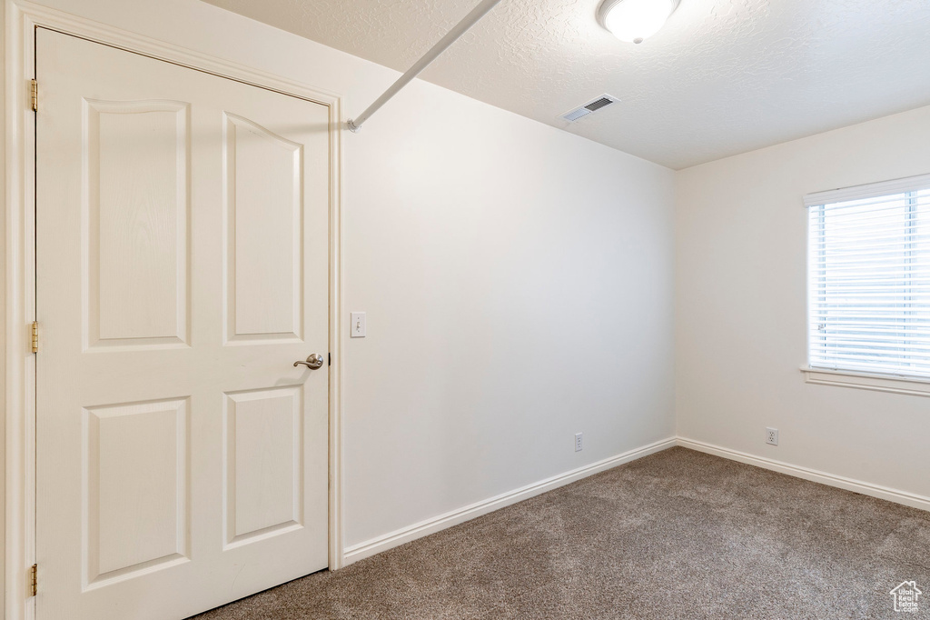 Carpeted spare room featuring baseboards, a textured ceiling, and visible vents