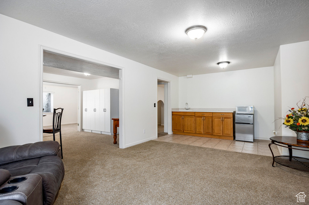 Living area with light colored carpet, a textured ceiling, baseboards, arched walkways, and light tile patterned flooring
