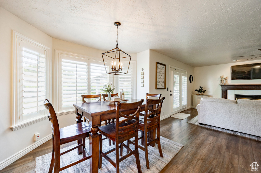 Dining room with a textured ceiling, baseboards, a chandelier, dark wood finished floors, and a fireplace