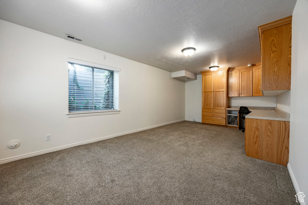 Unfurnished living room featuring carpet, baseboards, and a textured ceiling