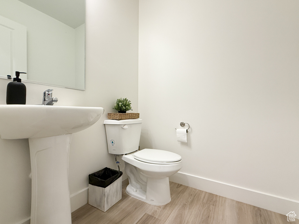 Half bathroom with baseboards, wood finished floors, and toilet