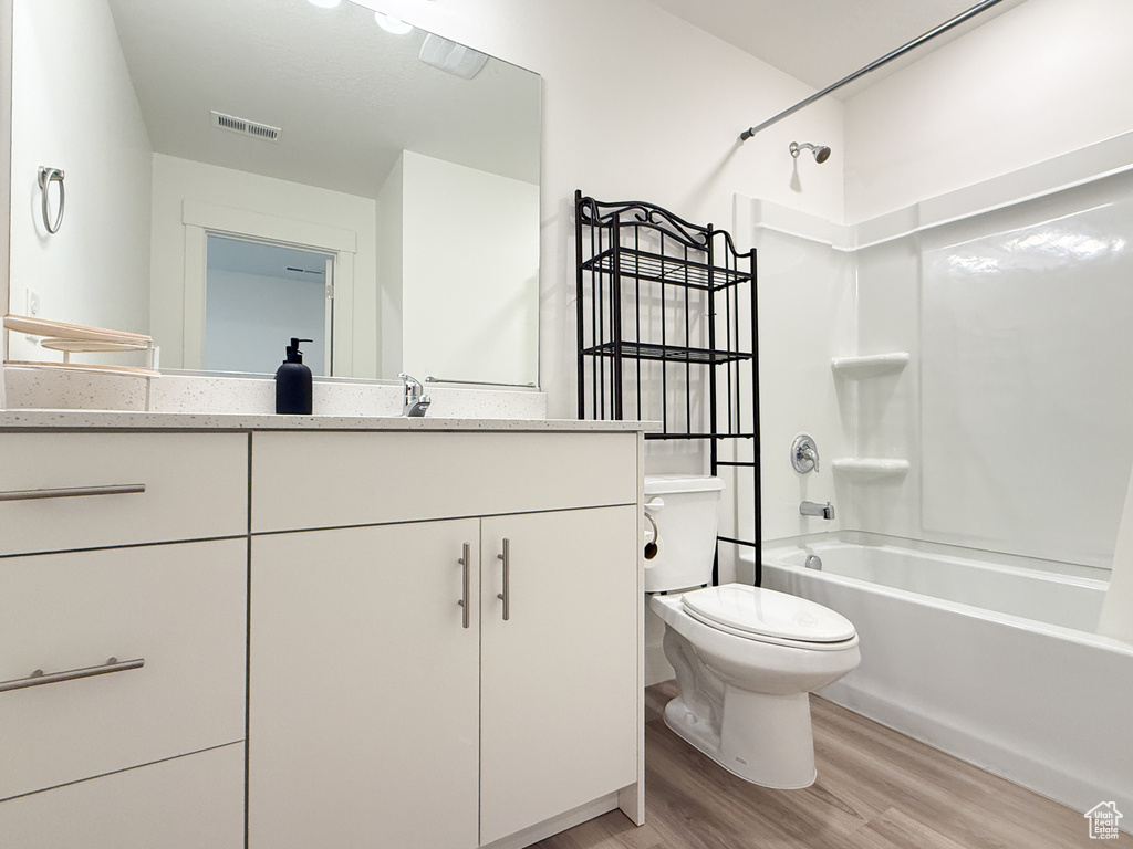 Full bathroom with visible vents, vanity, wood finished floors, toilet, and shower / tub combination