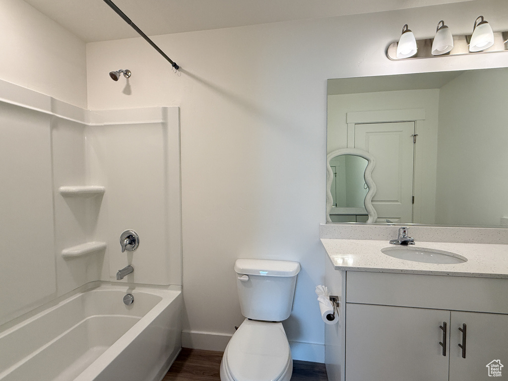 Full bath with shower / bathing tub combination, wood finished floors, baseboards, vanity, and toilet