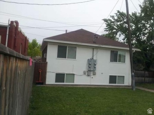 Rear view of house with a lawn, fence, and stucco siding