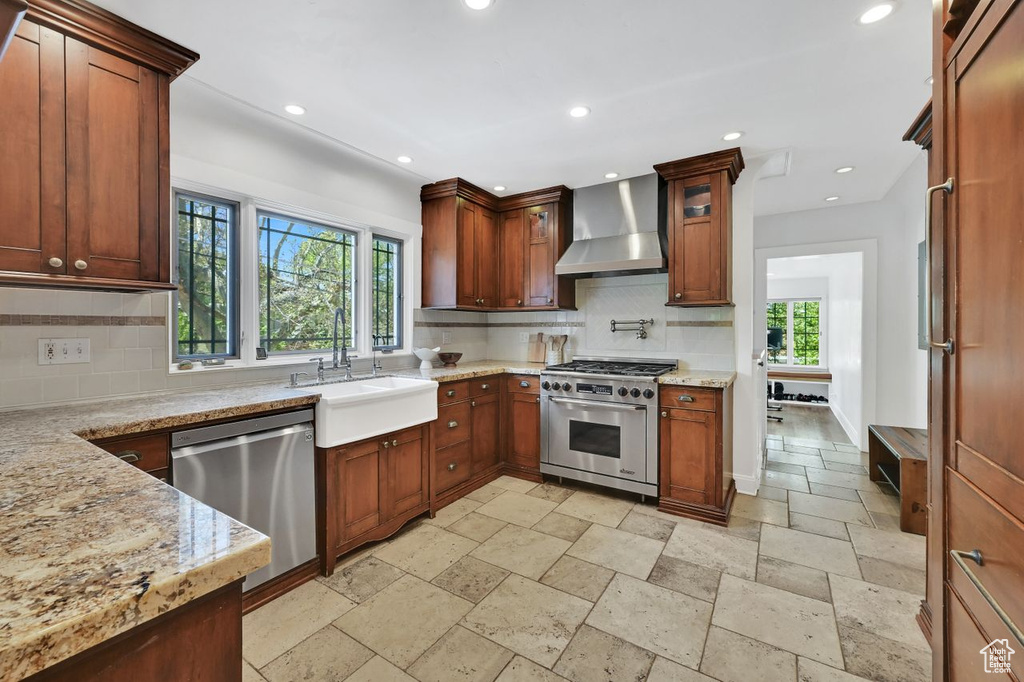 Kitchen featuring wall chimney range hood, appliances with stainless steel finishes, a wealth of natural light, and a sink