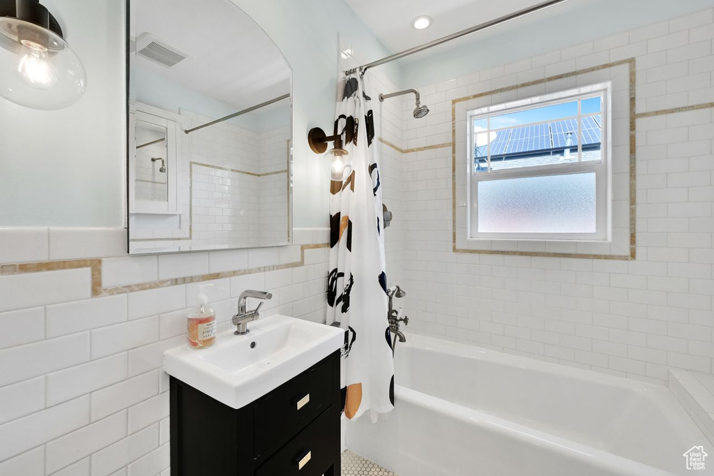 Full bathroom with visible vents, vanity, shower / bath combo with shower curtain, and tile walls