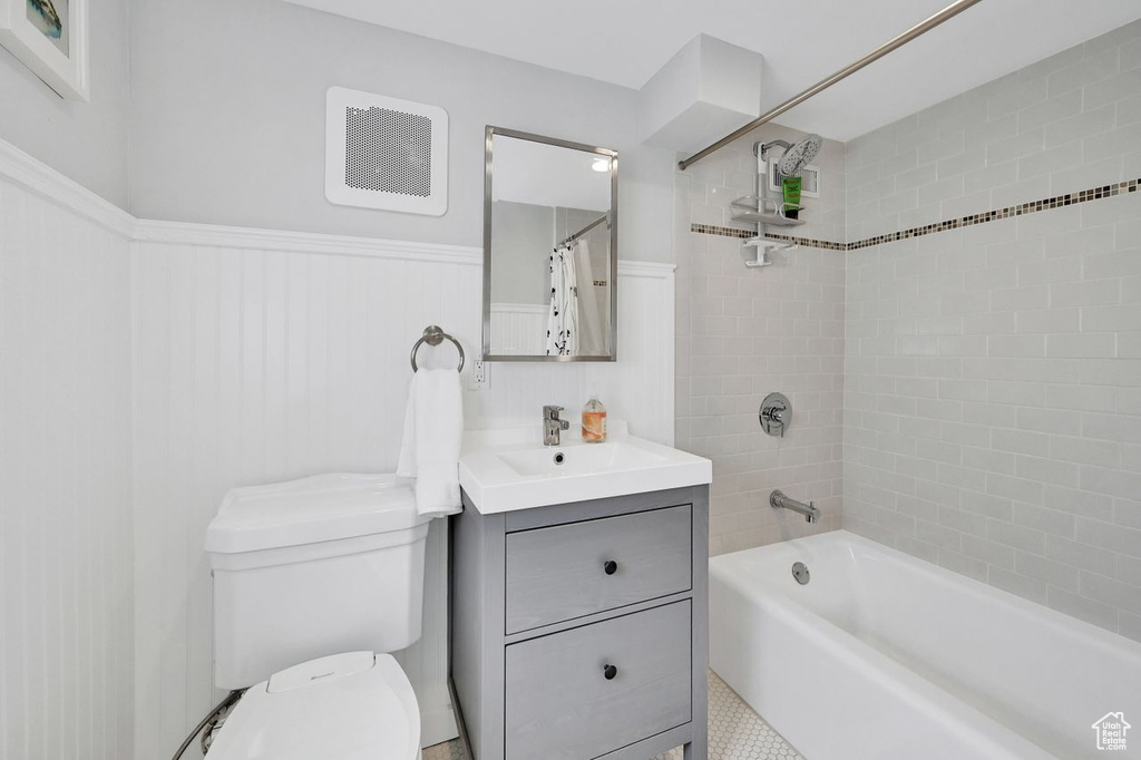 Full bathroom with visible vents, shower / bath combo with shower curtain, wainscoting, vanity, and toilet