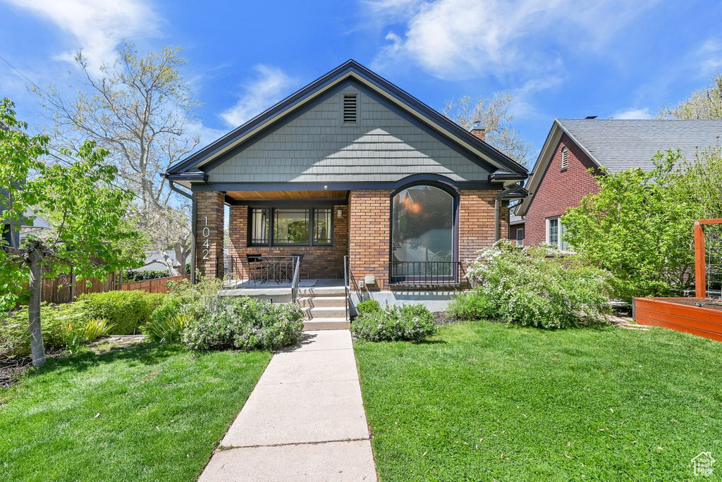 View of front of property with brick siding, a front lawn, fence, and covered porch