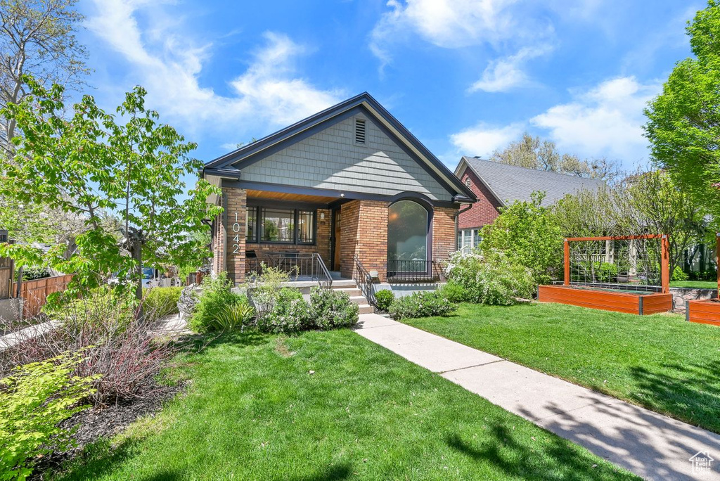 View of front facade with covered porch, brick siding, a garden, and a front lawn