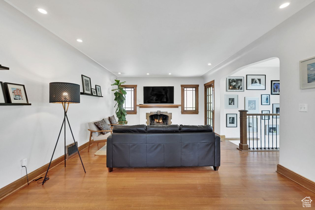 Living room featuring a warm lit fireplace, arched walkways, recessed lighting, baseboards, and wood finished floors