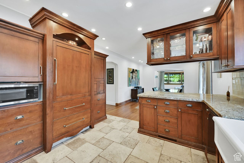 Kitchen featuring stone tile floors, a peninsula, recessed lighting, stainless steel microwave, and arched walkways