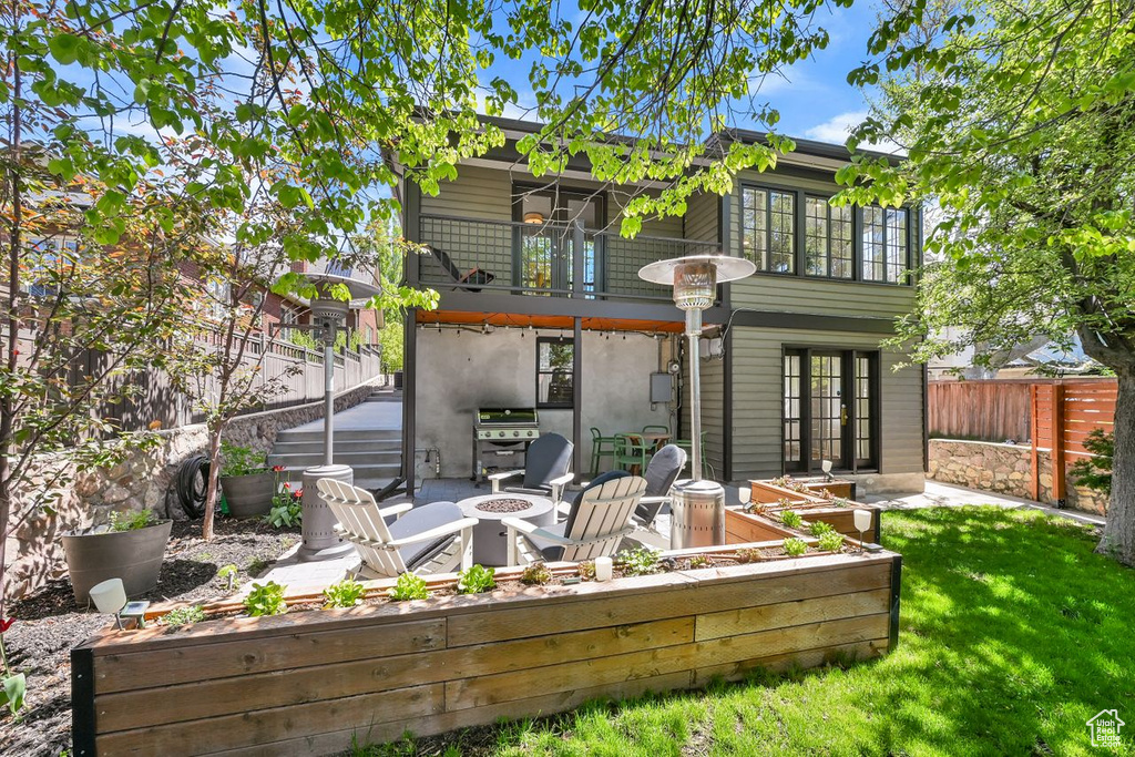 Back of house featuring fence, an outdoor fire pit, stucco siding, a balcony, and a lawn