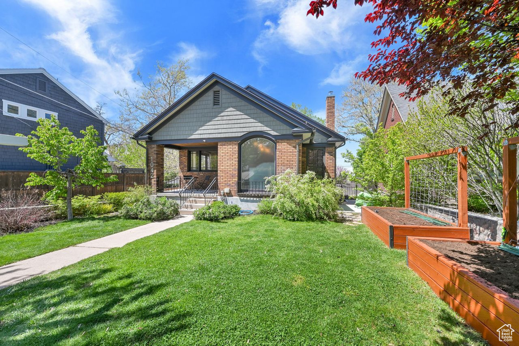 Rear view of house featuring brick siding, a porch, a vegetable garden, a chimney, and a yard