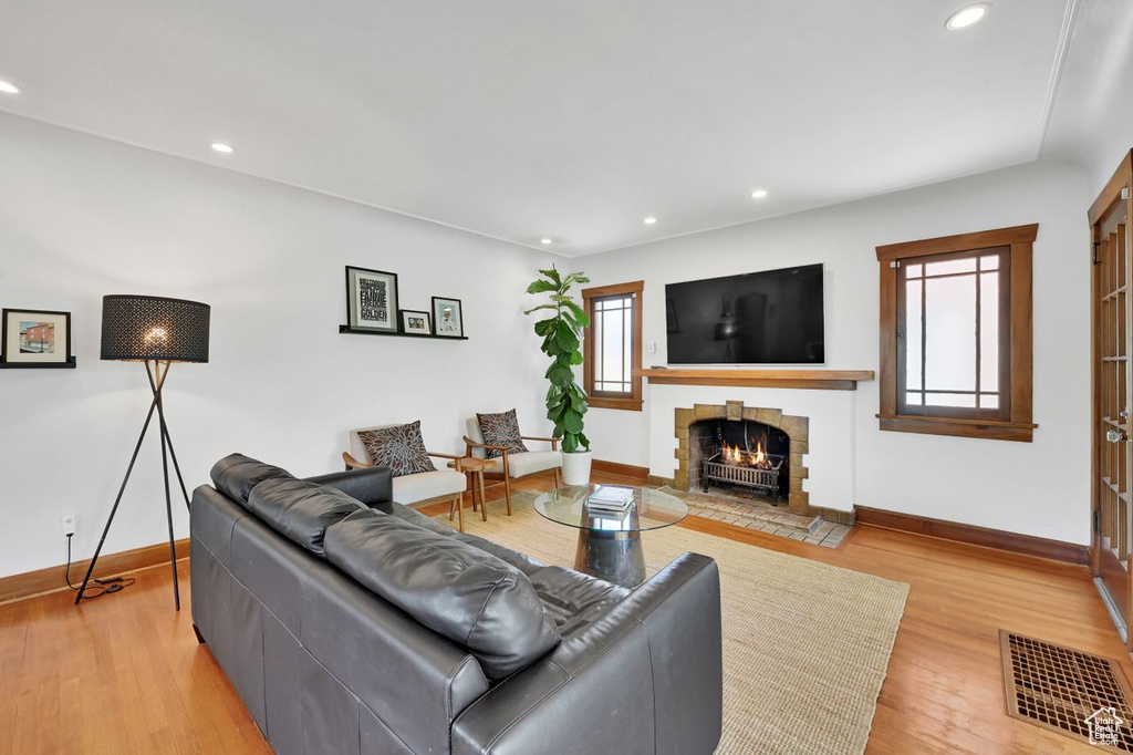 Living area with a lit fireplace, visible vents, baseboards, light wood-style floors, and recessed lighting