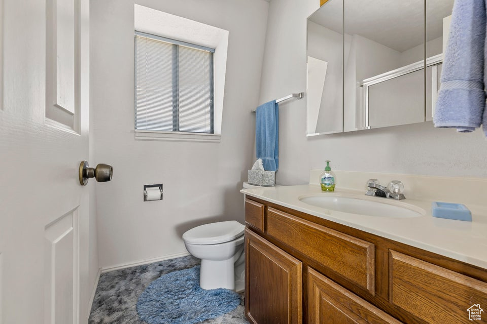 Full bath featuring vanity, baseboards, a shower with door, and toilet