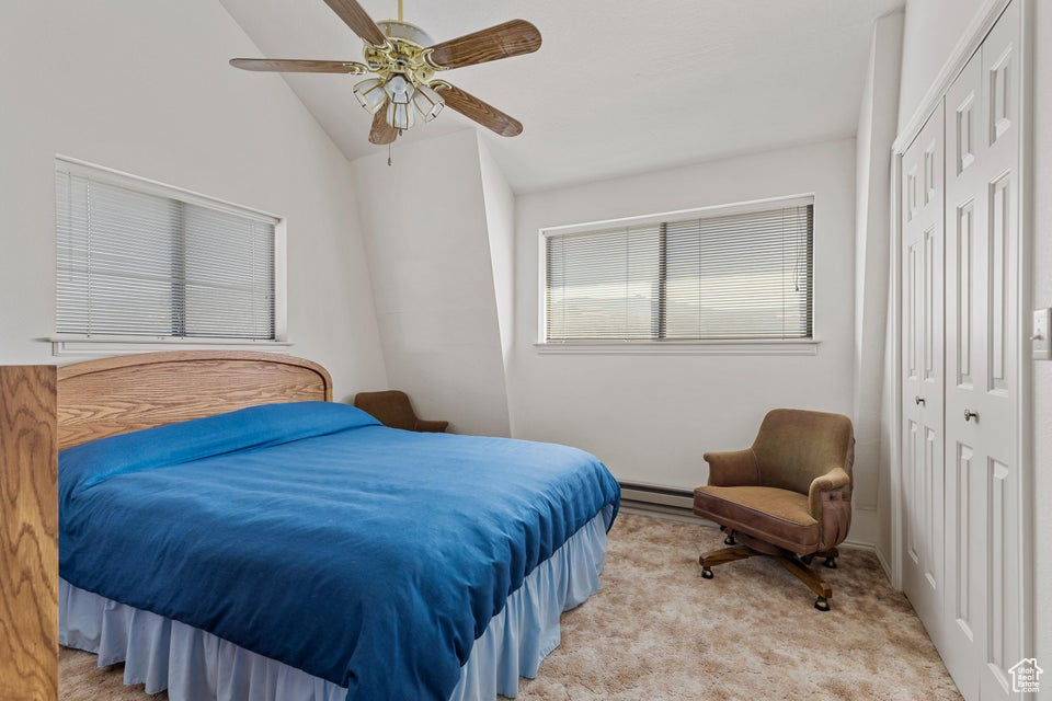 Bedroom featuring ceiling fan, light carpet, a baseboard radiator, vaulted ceiling, and a closet