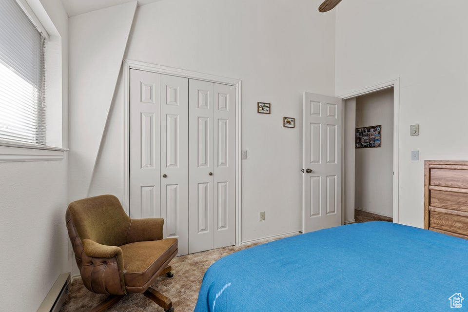 Carpeted bedroom featuring baseboard heating, a closet, and a towering ceiling