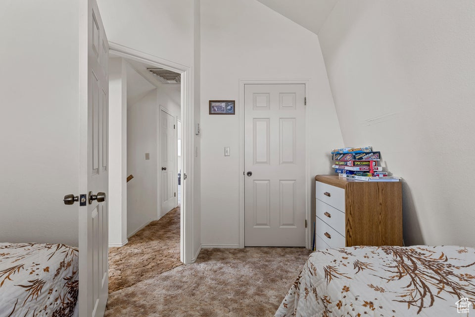 Bedroom with visible vents, baseboards, light colored carpet, and lofted ceiling