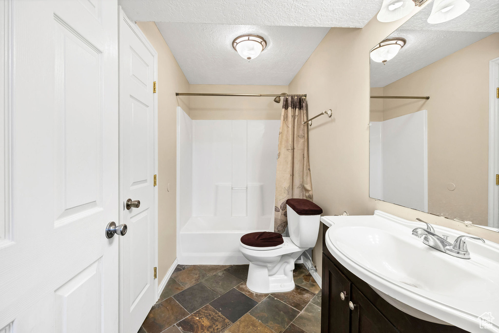 Full bathroom featuring vanity, toilet, a textured ceiling, stone tile floors, and baseboards