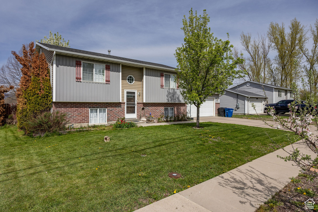 Split foyer home featuring a garage, driveway, a front lawn, and brick siding