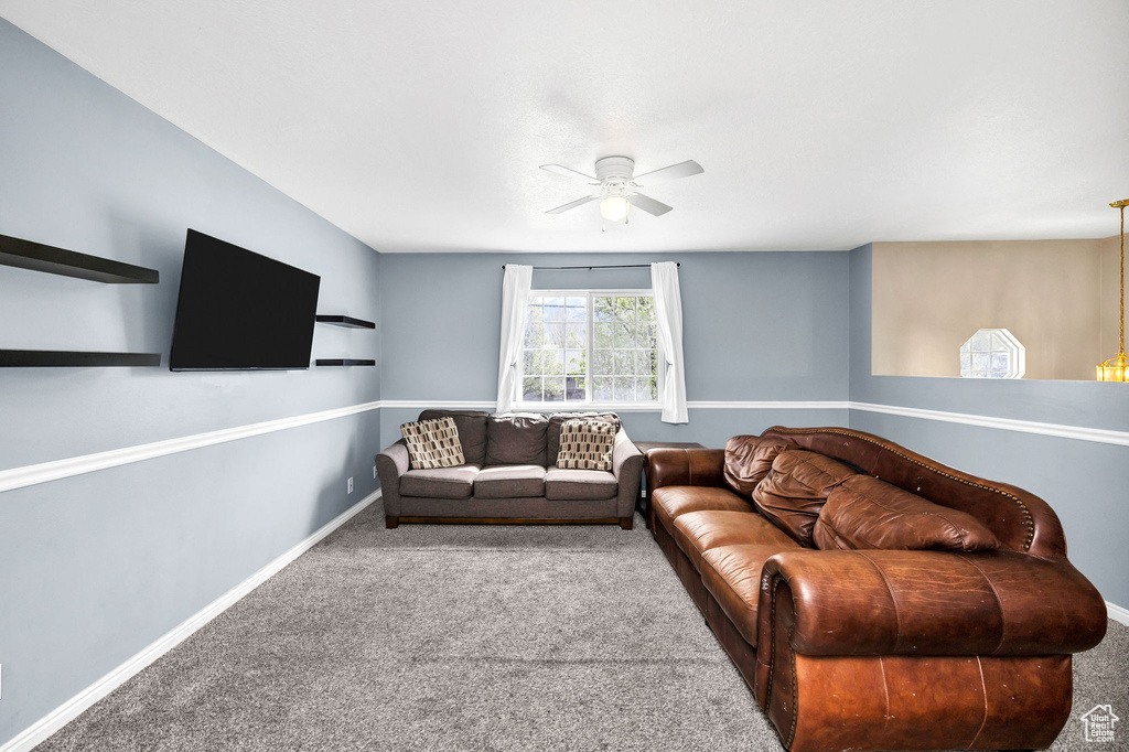 Carpeted living room featuring a ceiling fan and baseboards