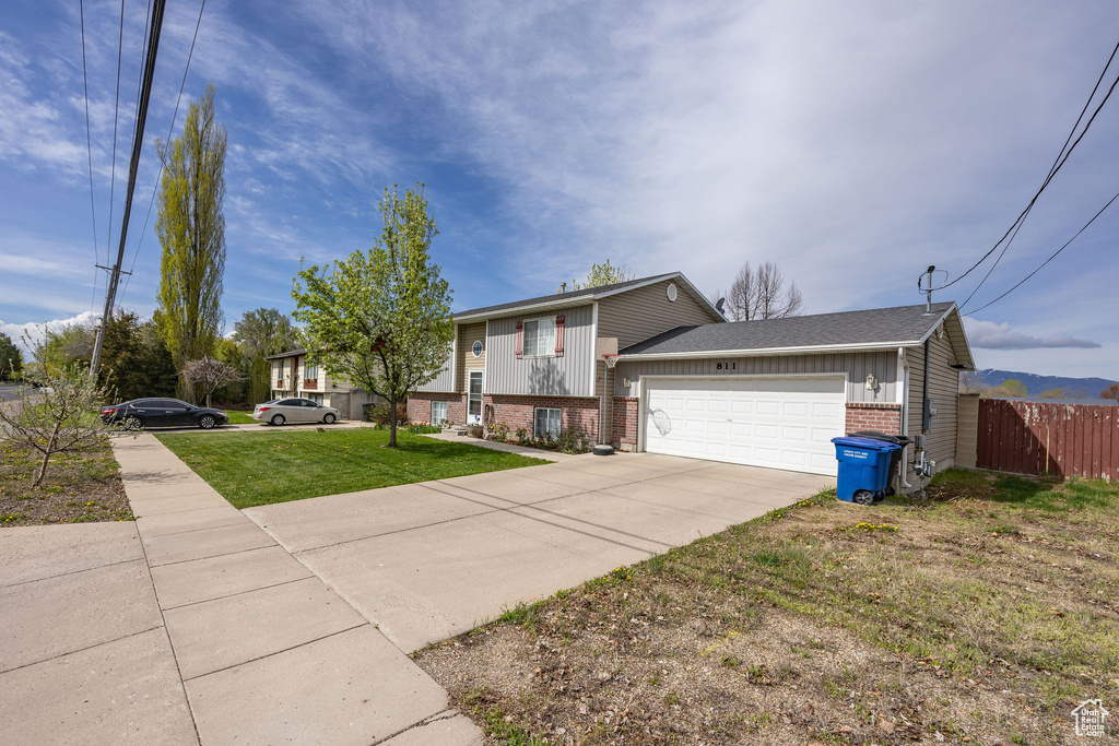 View of front of property featuring fence, brick siding, a garage, a front yard, and driveway