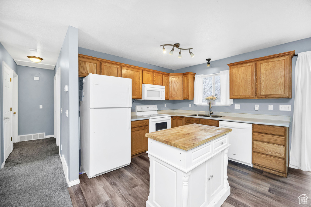 Kitchen featuring white appliances, dark wood-style flooring, a kitchen island, and a sink