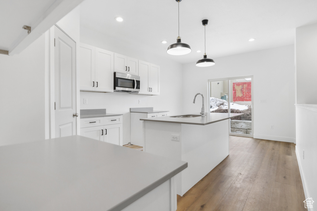 Kitchen featuring stainless steel microwave, white cabinets, light wood-style flooring, a sink, and a kitchen island with sink