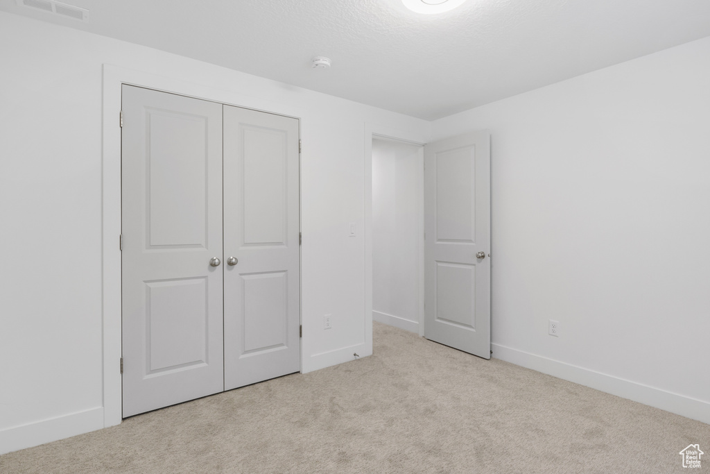 Unfurnished bedroom featuring baseboards, visible vents, light carpet, and a closet