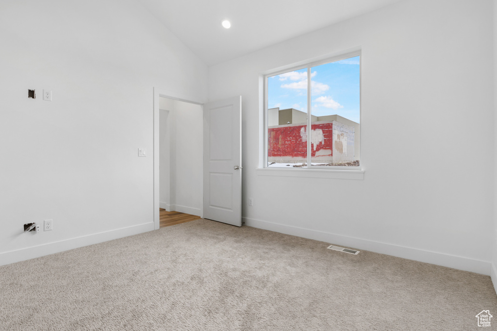 Carpeted spare room with visible vents, vaulted ceiling, and baseboards