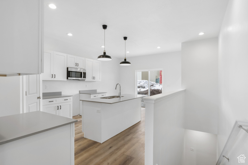 Kitchen featuring light wood finished floors, stainless steel microwave, white cabinets, and a sink