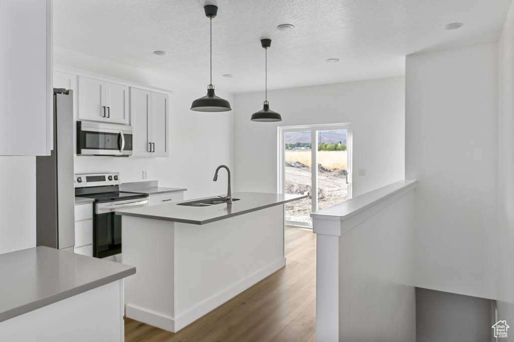 Kitchen featuring stainless steel appliances, a sink, white cabinetry, light wood-type flooring, and pendant lighting