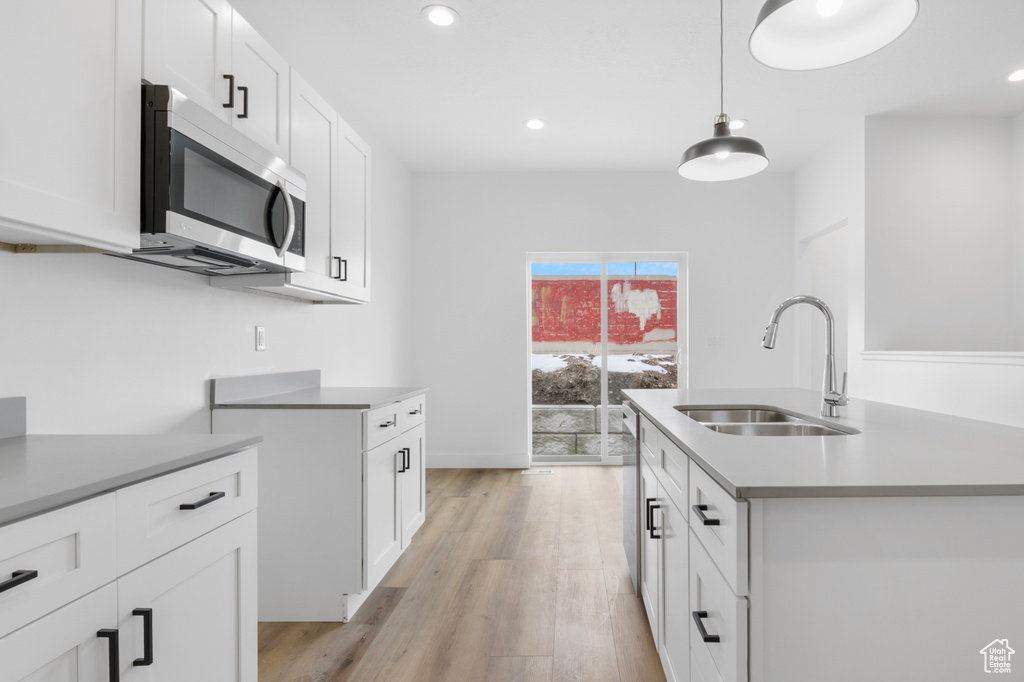 Kitchen featuring recessed lighting, stainless steel appliances, white cabinets, a sink, and light wood-type flooring