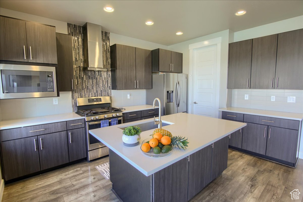 Kitchen featuring wall chimney range hood, a sink, light countertops, stainless steel appliances, and tasteful backsplash